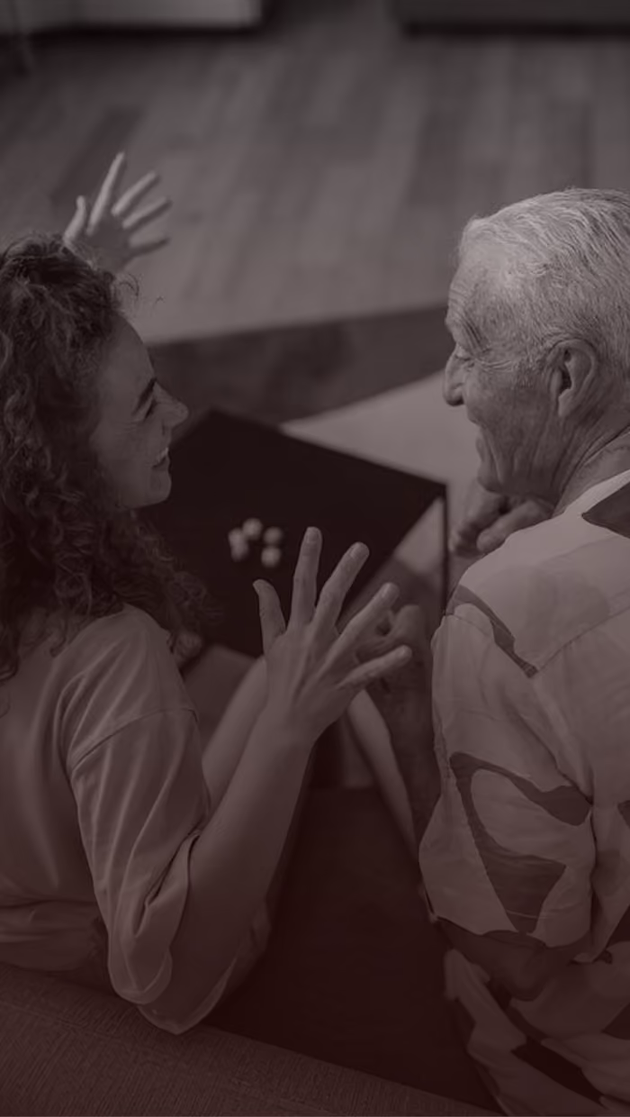 Smiling elderly man and young woman sitting facing each other, gesturing with their hands.