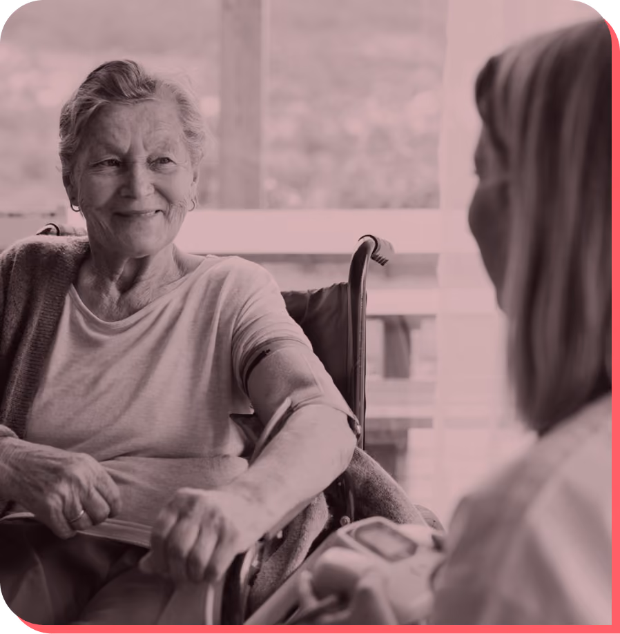 Smiling elderly woman in wheelchair having her blood pressure taken by a healthcare professional.