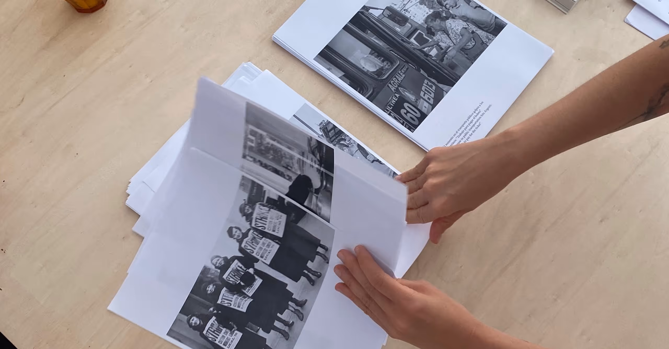 Hands flipping through printed black-and-white photos on a wooden table.