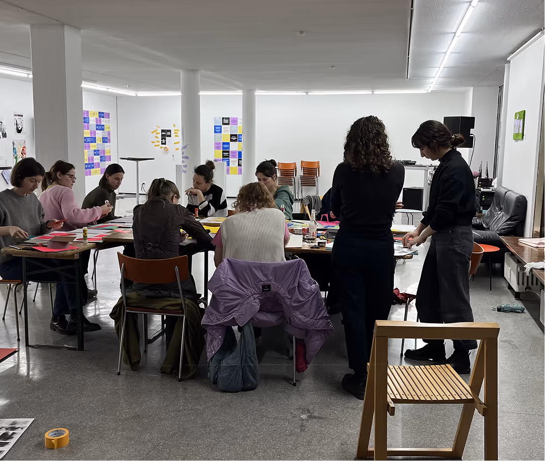Group of people engaged in a workshop around a large table with papers and art supplies in a bright room.