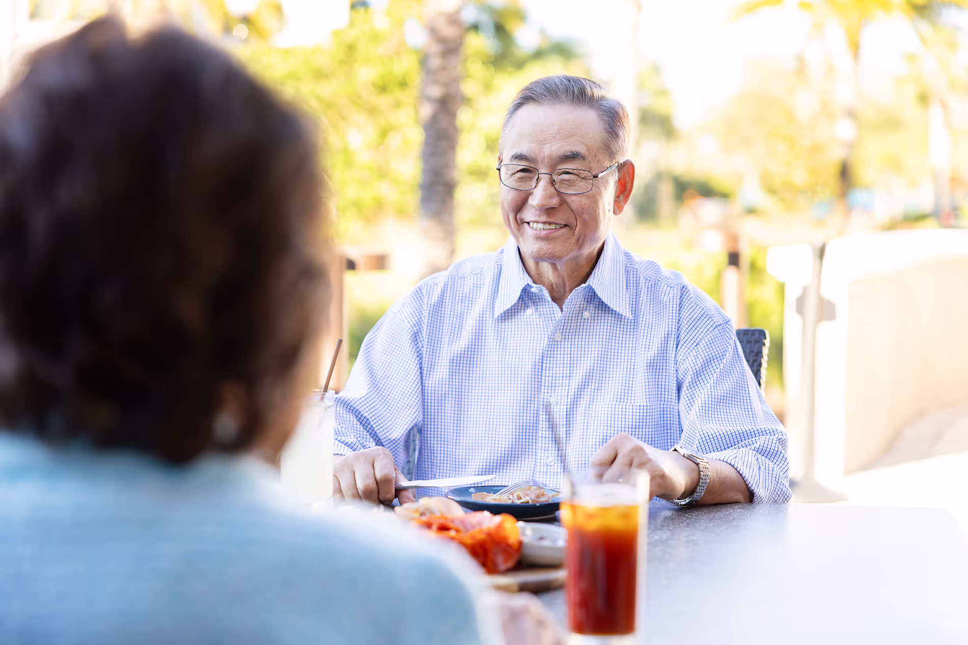 Asian older man and his wife enjoying a meal and sipping tea together on an outdoor patio, sharing a peaceful moment in a cozy setting.