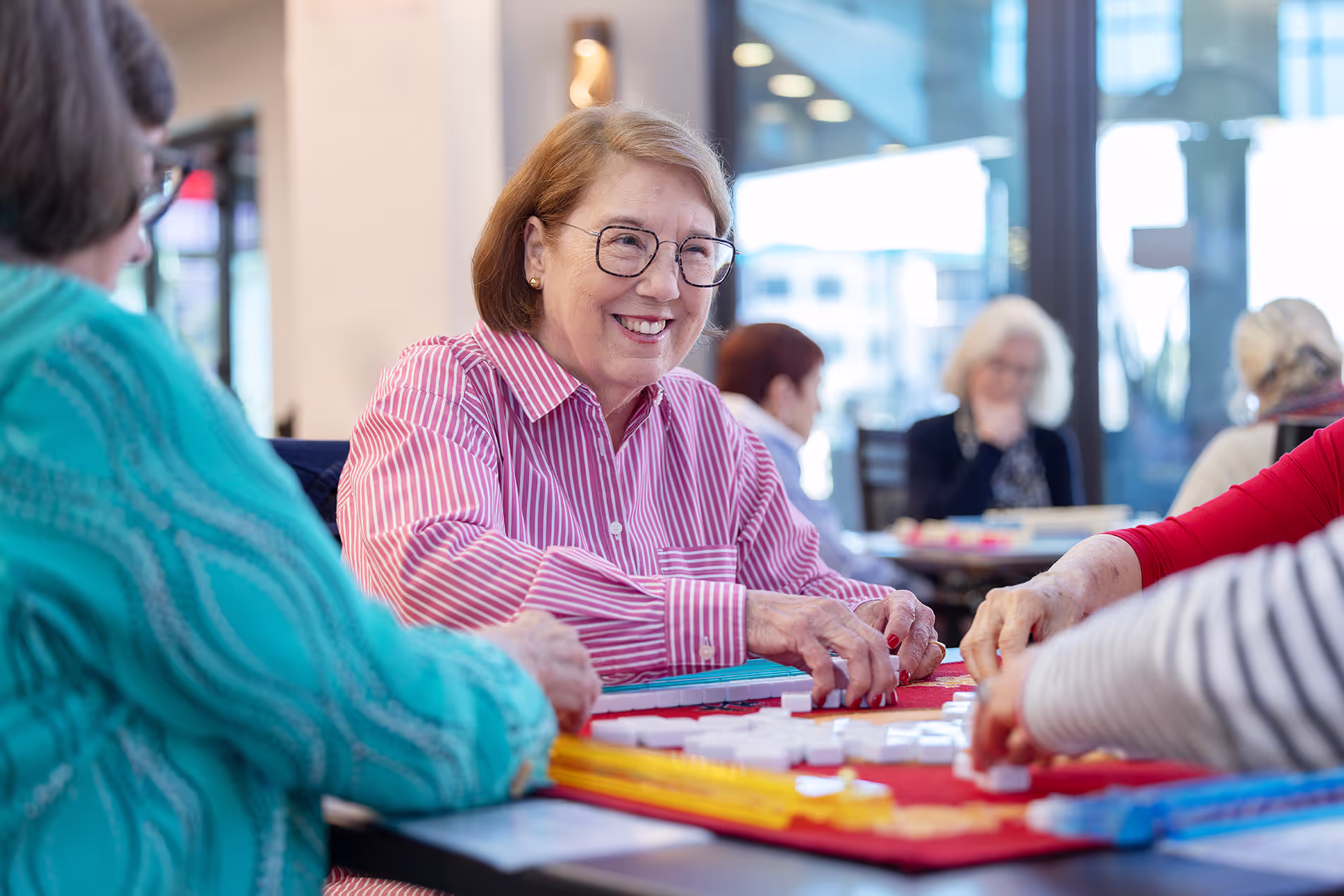 Group of seniors smiling and playing Mahjong together, enjoying a lively and engaging game in a social setting.