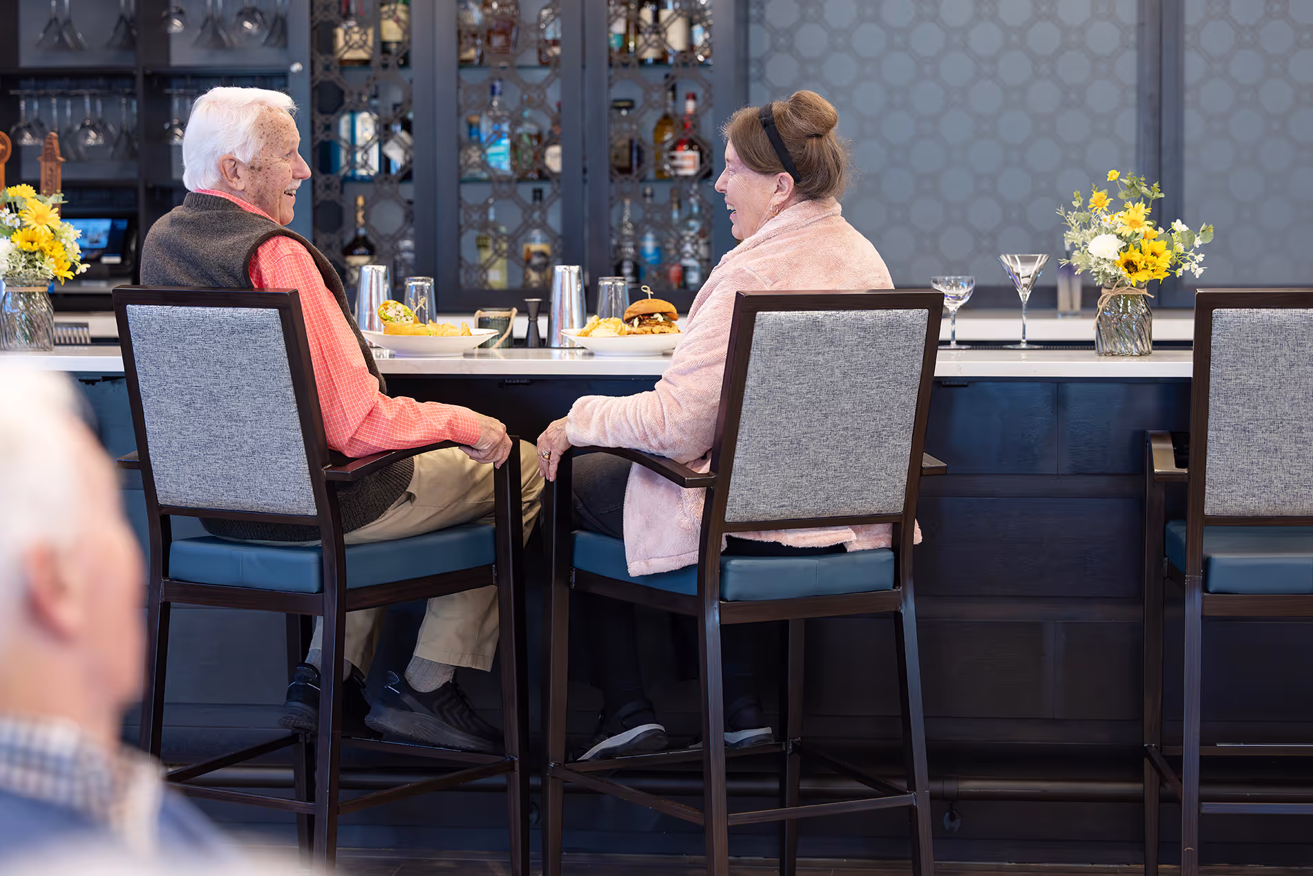 Senior couple sitting at the bar, enjoying each other's company with smiles and conversation in a cozy, relaxed setting.