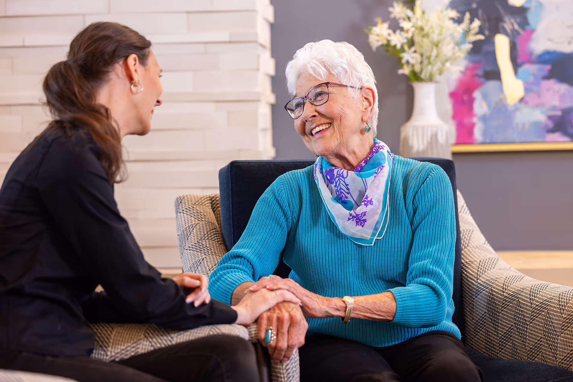 Staff member and resident sharing a meaningful moment, looking at each other's hands, symbolizing care and connection.