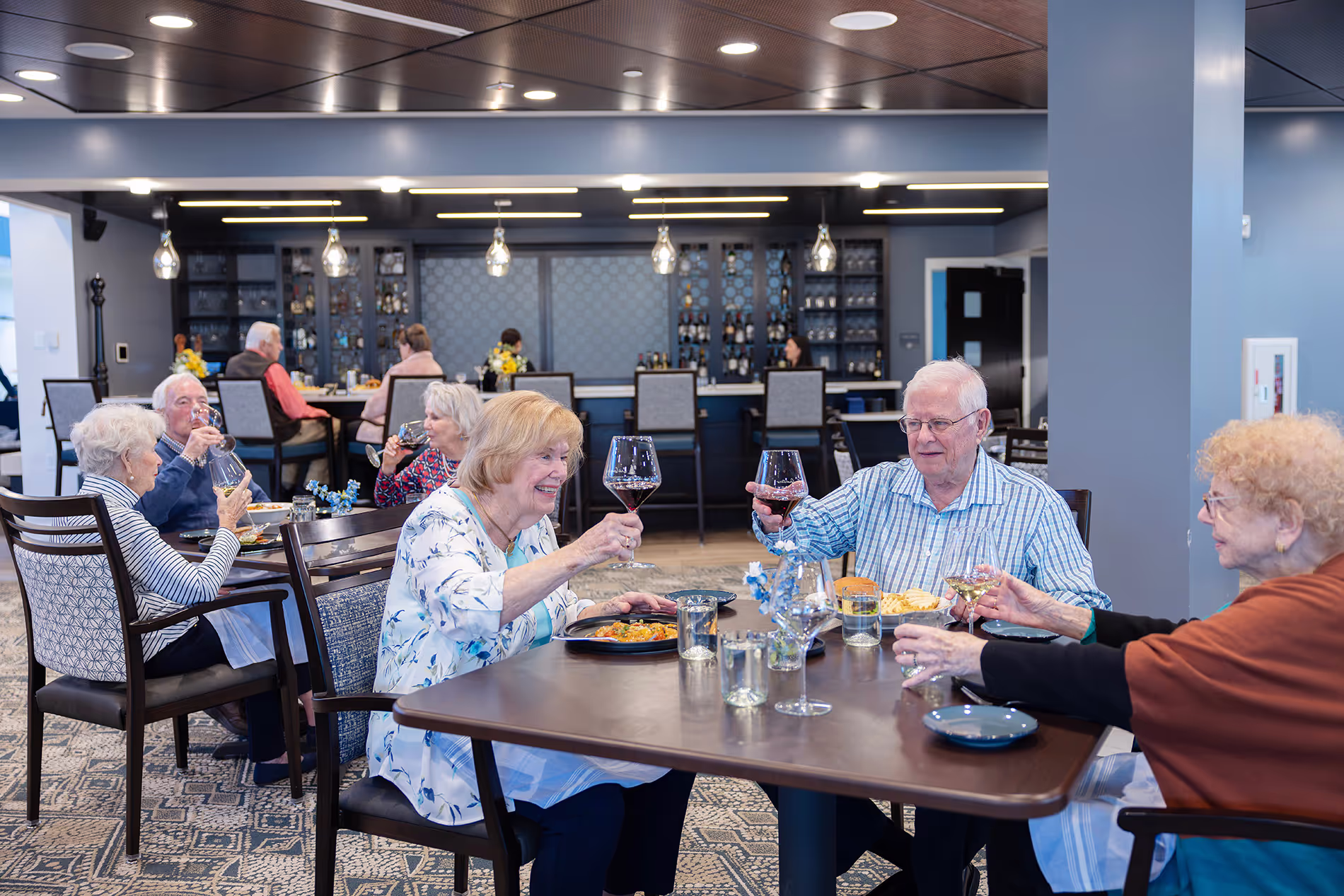 People dining together in the main dining room, enjoying conversation and meals in a bright, welcoming atmosphere with elegant table settings.