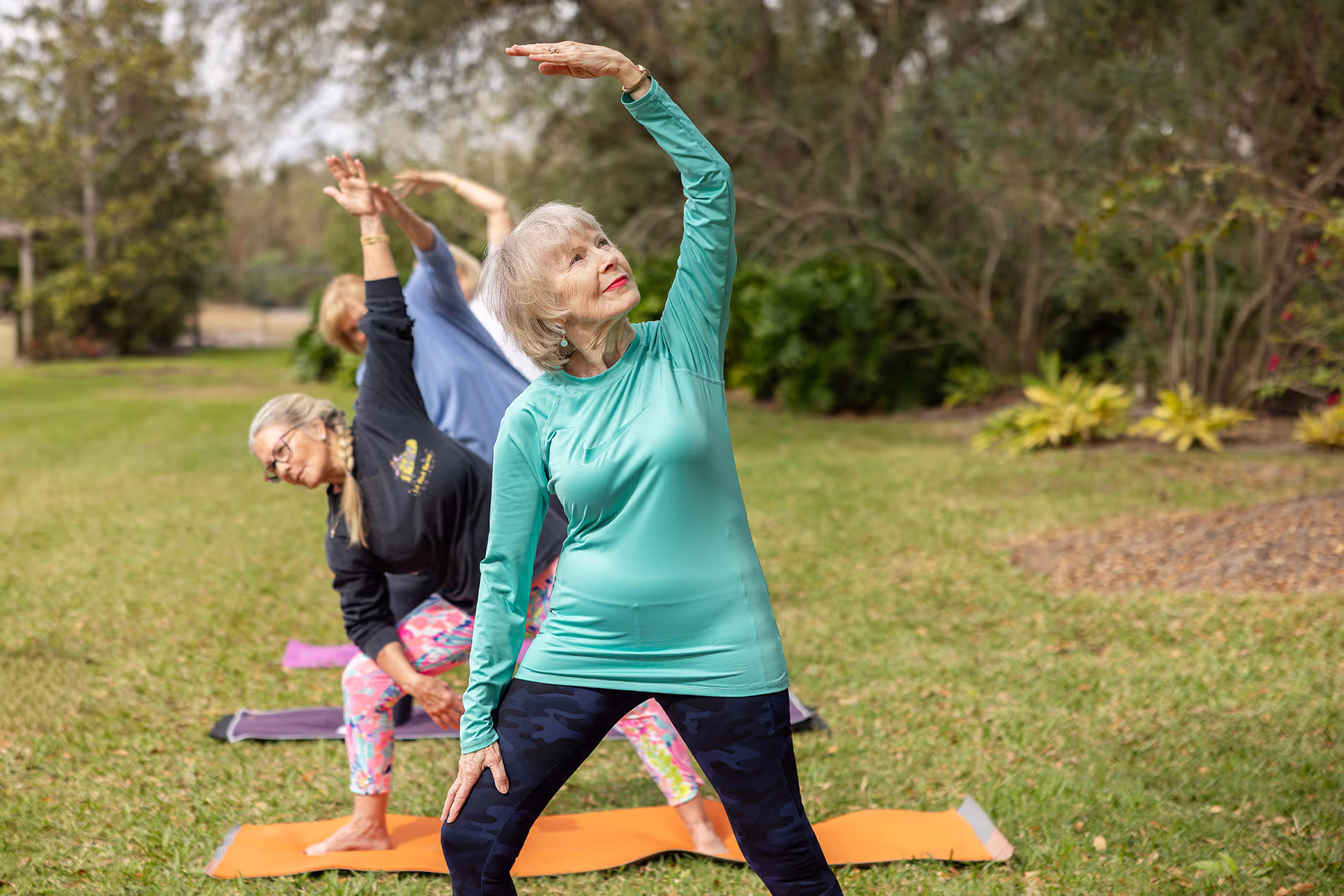 People practicing yoga outside on mats, surrounded by greenery and fresh air in a calm, natural setting.