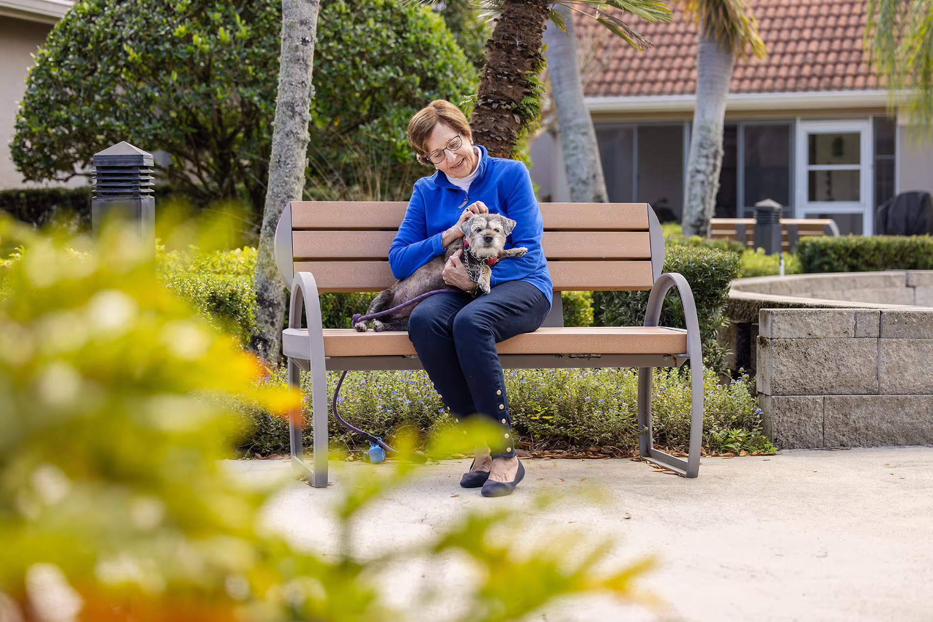 Older woman sitting on a bench with her dog by her side, enjoying a quiet moment together in a peaceful outdoor setting.