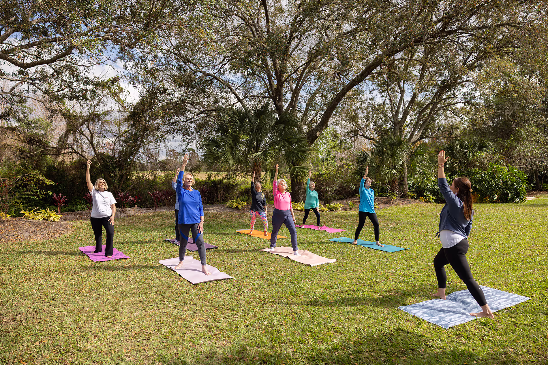 Group of individuals participating in a yoga class outdoors, practicing poses on mats in a peaceful, natural setting with clear skies and greenery around them.