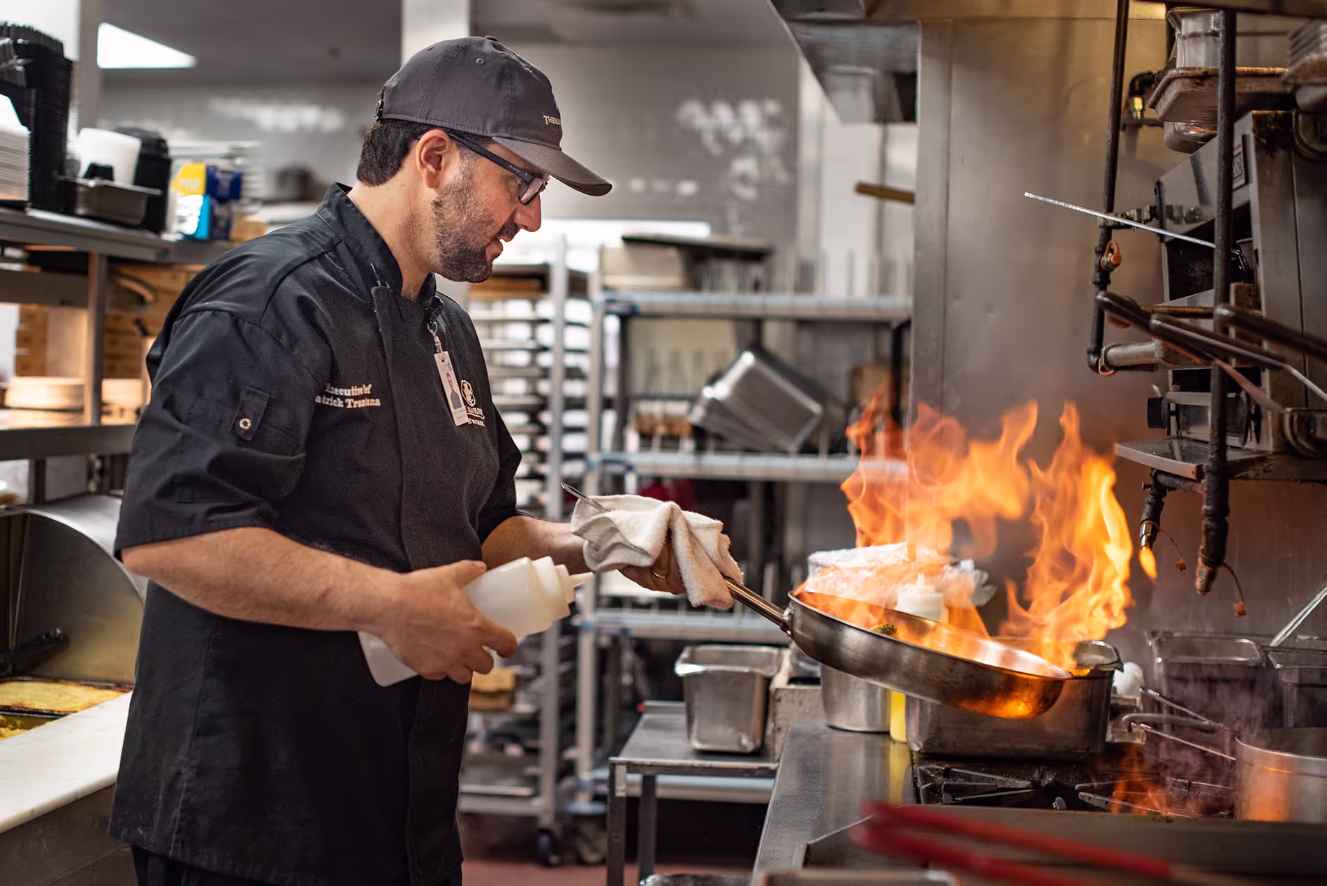 Chef cooking in a spacious kitchen, skillfully working with a flame from a stove, creating a dynamic cooking moment surrounded by professional kitchen tools.