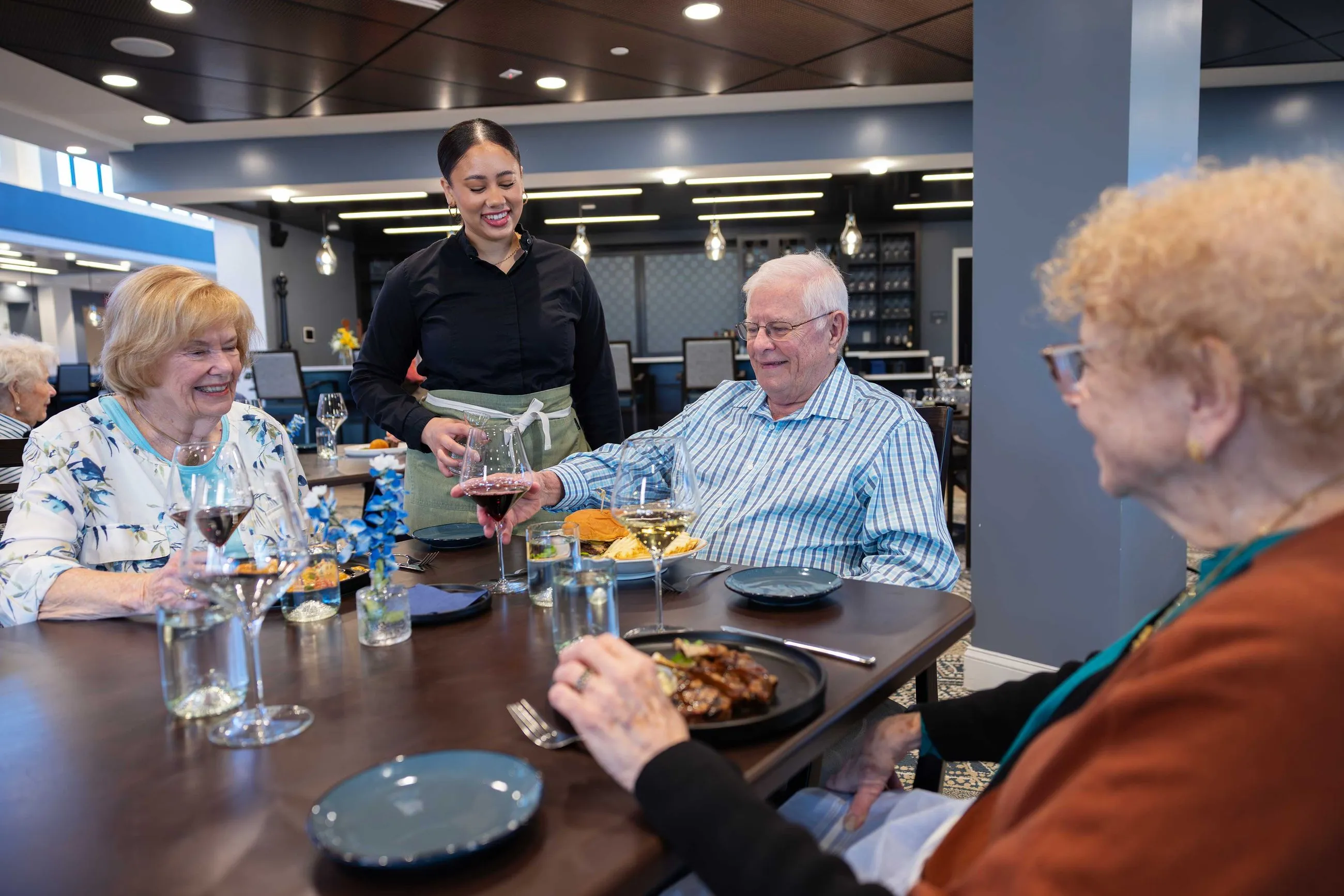 Server assisting a table of older adults, smiling and engaging in friendly conversation while taking their order.