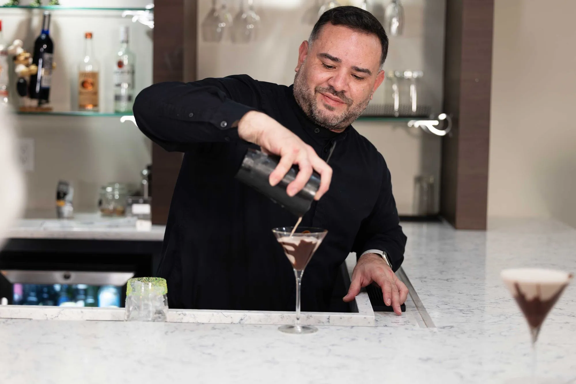Server skillfully preparing a chocolaty cocktail, carefully pouring ingredients into a glass with a focused expression.