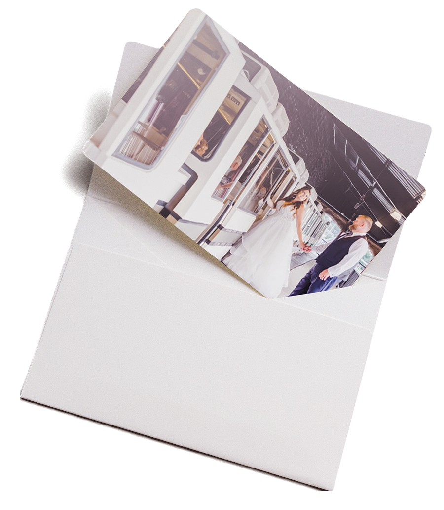 Photo of a bride in white dress and groom holding hands on a train platform inside a white envelope.