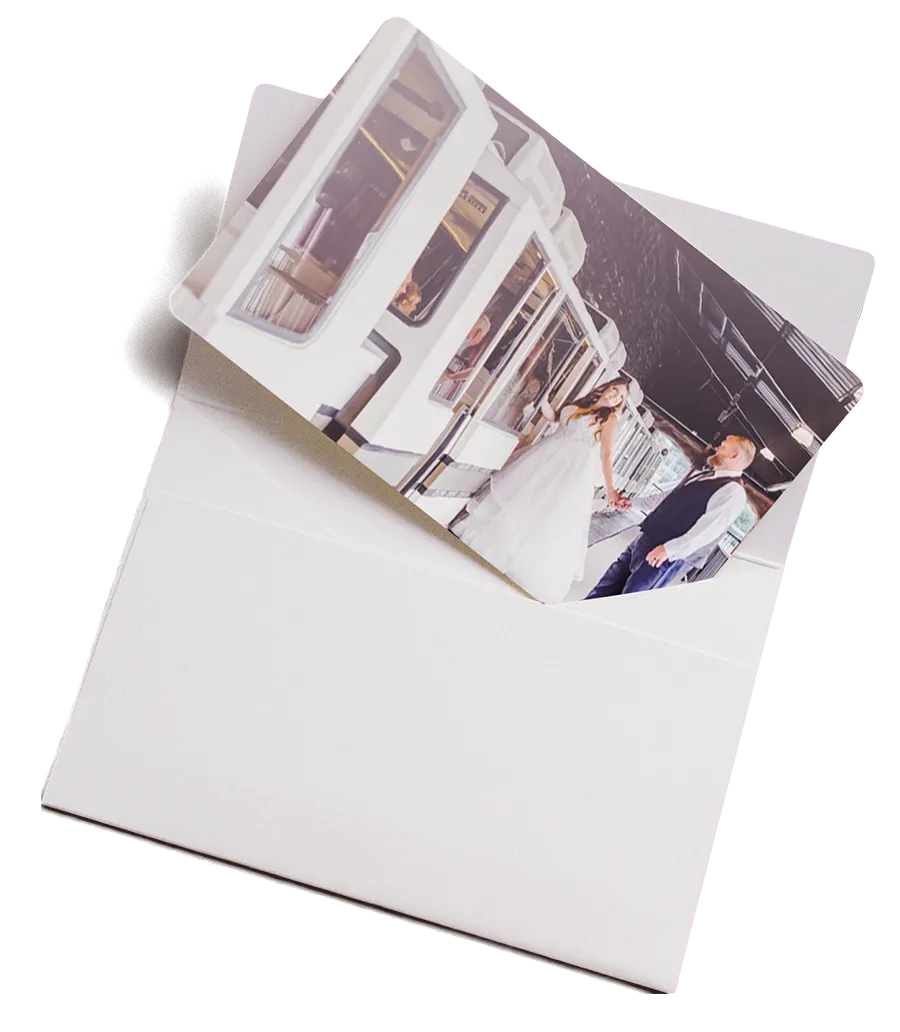 Photo of a bride in white dress and groom holding hands on a train platform inside a white envelope.
