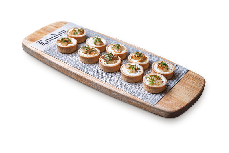 Wooden platter with ten small tart appetizers garnished with herbs on printed paper.