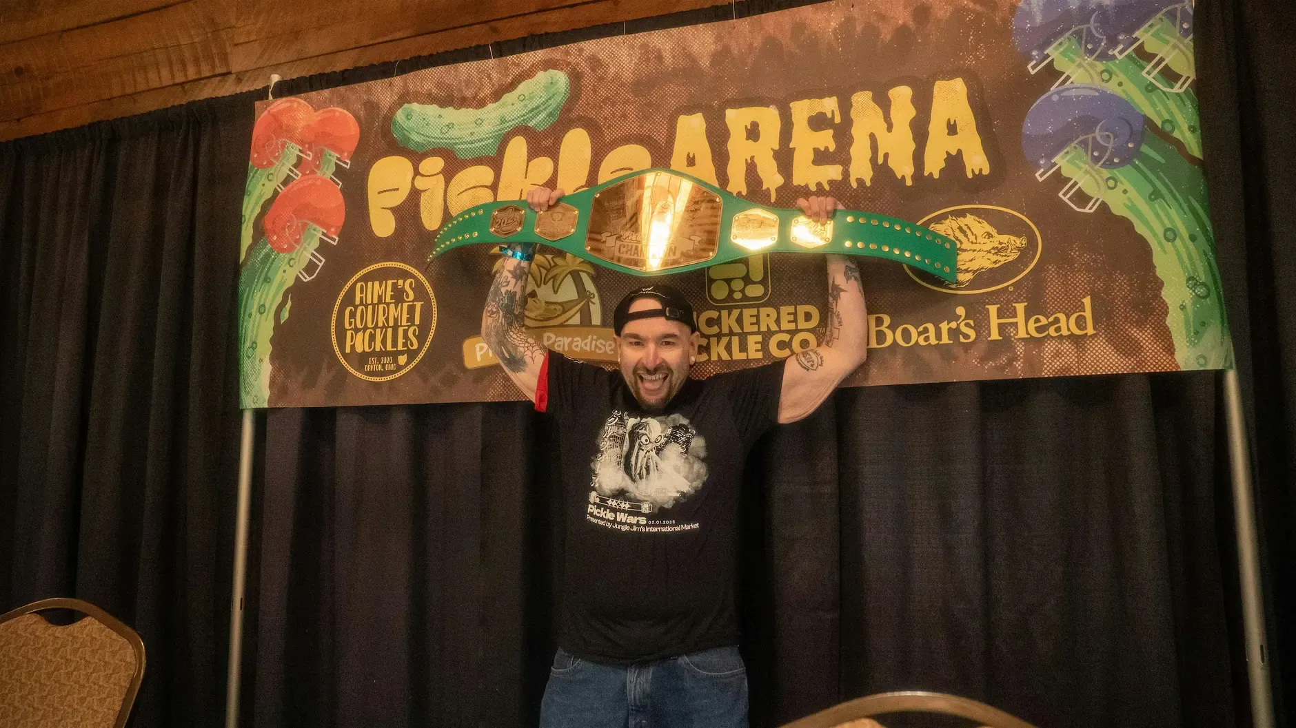Pickle Wars participant posing in front of the Pickle Arena banner
