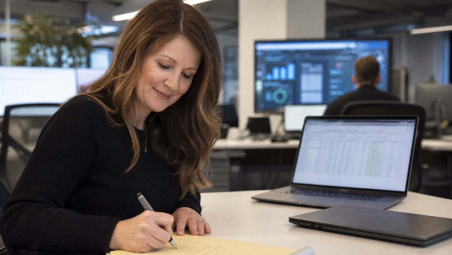 Woman notes cloud costs on legal pad, laptop screen visible