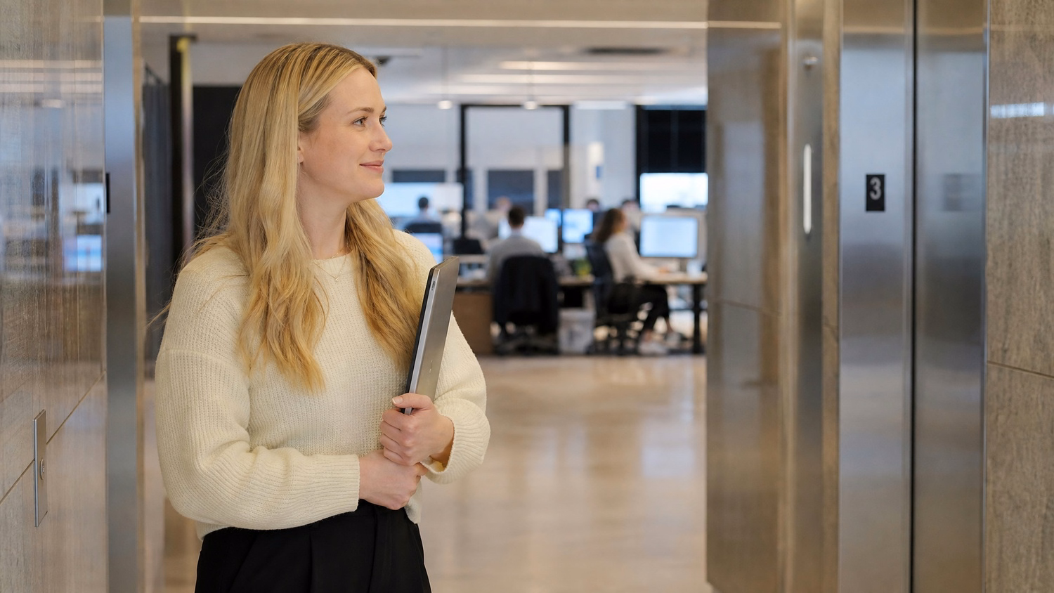 Woman with laptop waits in modern elevator lobby