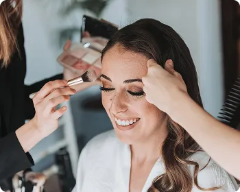 Smiling woman having makeup applied by two artists using brushes.