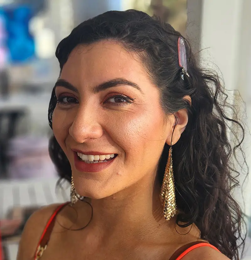 Woman with curly hair and glamorous event makeup smiling at camera