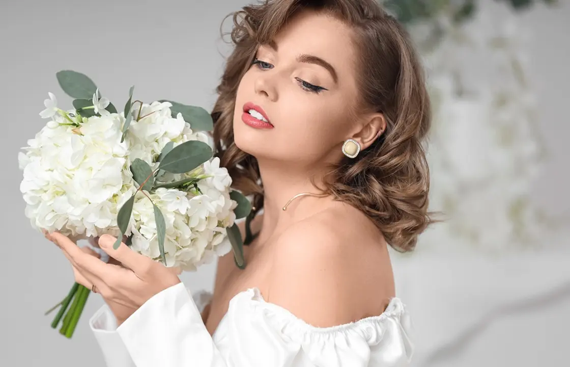 Elegant bride-inspired model with soft glam makeup holding white flower bouquet