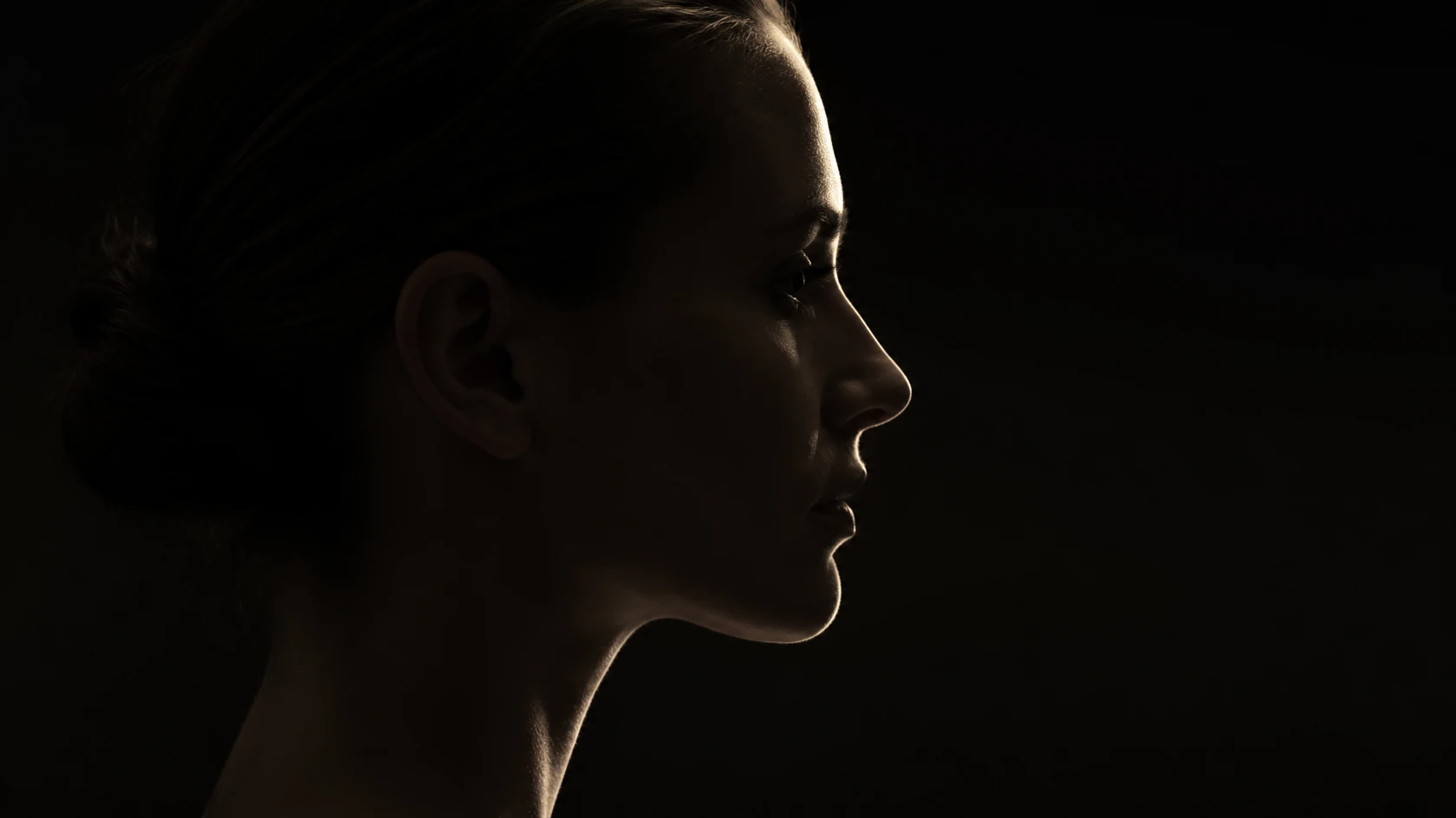 Side profile of a woman in low light, with a thin rim of light along her forehead, nose, chin and neck, the features this guide puts in order of priority.