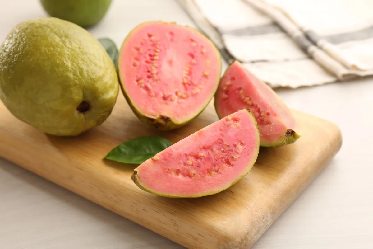 Pink guava halves and slices on a wooden cutting board