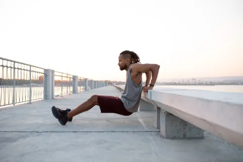 Man doing bench dips on a waterfront promenade