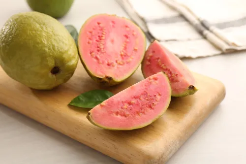 Pink guava halves and slices on a wooden cutting board