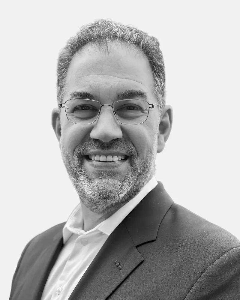 Smiling man with glasses, salt-and-pepper hair and beard, wearing a suit jacket and white shirt.