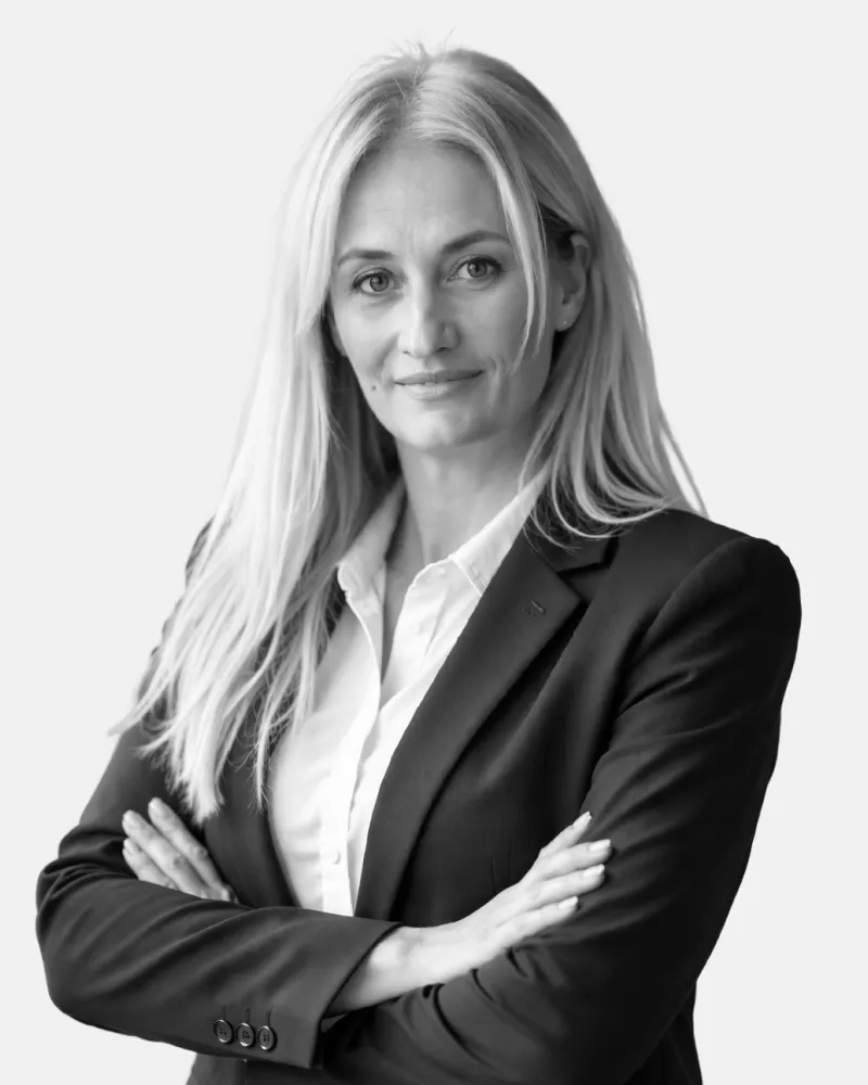 Confident woman with long hair in a suit jacket and white shirt standing with arms crossed.