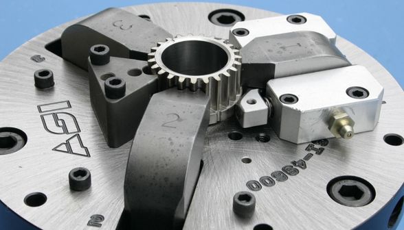 Close-up of a precision-machined metal part with a central gear and adjustable clamps on a circular plate.