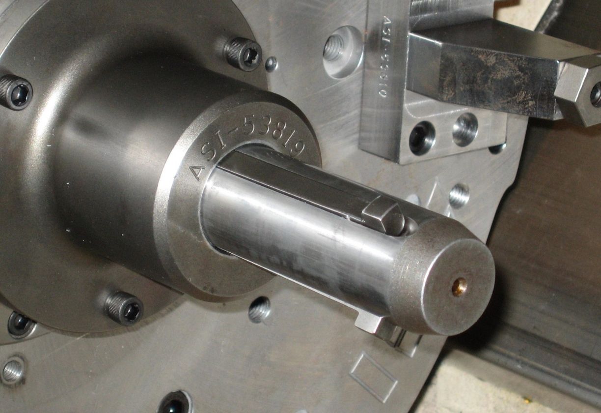 Close-up of a precision metal machining component marked with ASI-53819, mounted on industrial equipment.