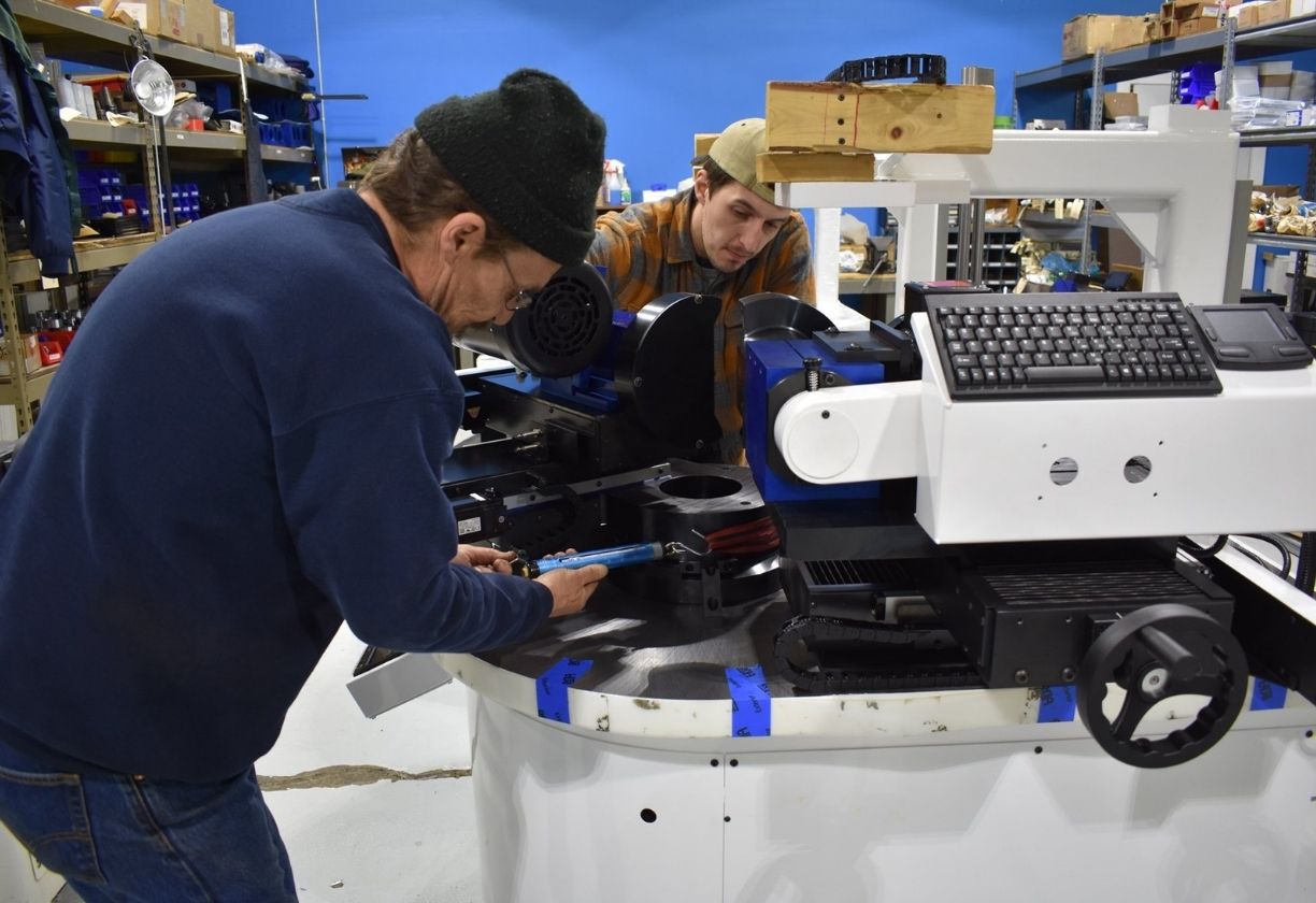 Two men working on a large industrial machine with a computer keyboard in a workshop.