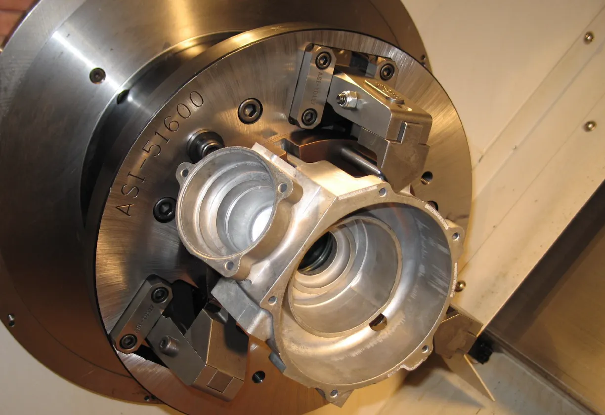 Close-up of a custom metal workholding chuck gripping a machined aluminum part inside industrial equipment.
