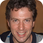 Smiling man with curly dark hair and light skin wearing a dark shirt and jacket.