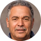 Portrait of a middle-aged man with gray hair, a mustache, and light brown skin wearing a dark shirt.