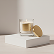 White coffee cup with coffee and a spoon on a beige coaster next to yellow cookies on a white surface.