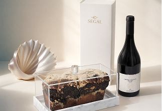 Clear container with marble loaf cake, white Segal box, black wine bottle, and a shell-shaped decoration.