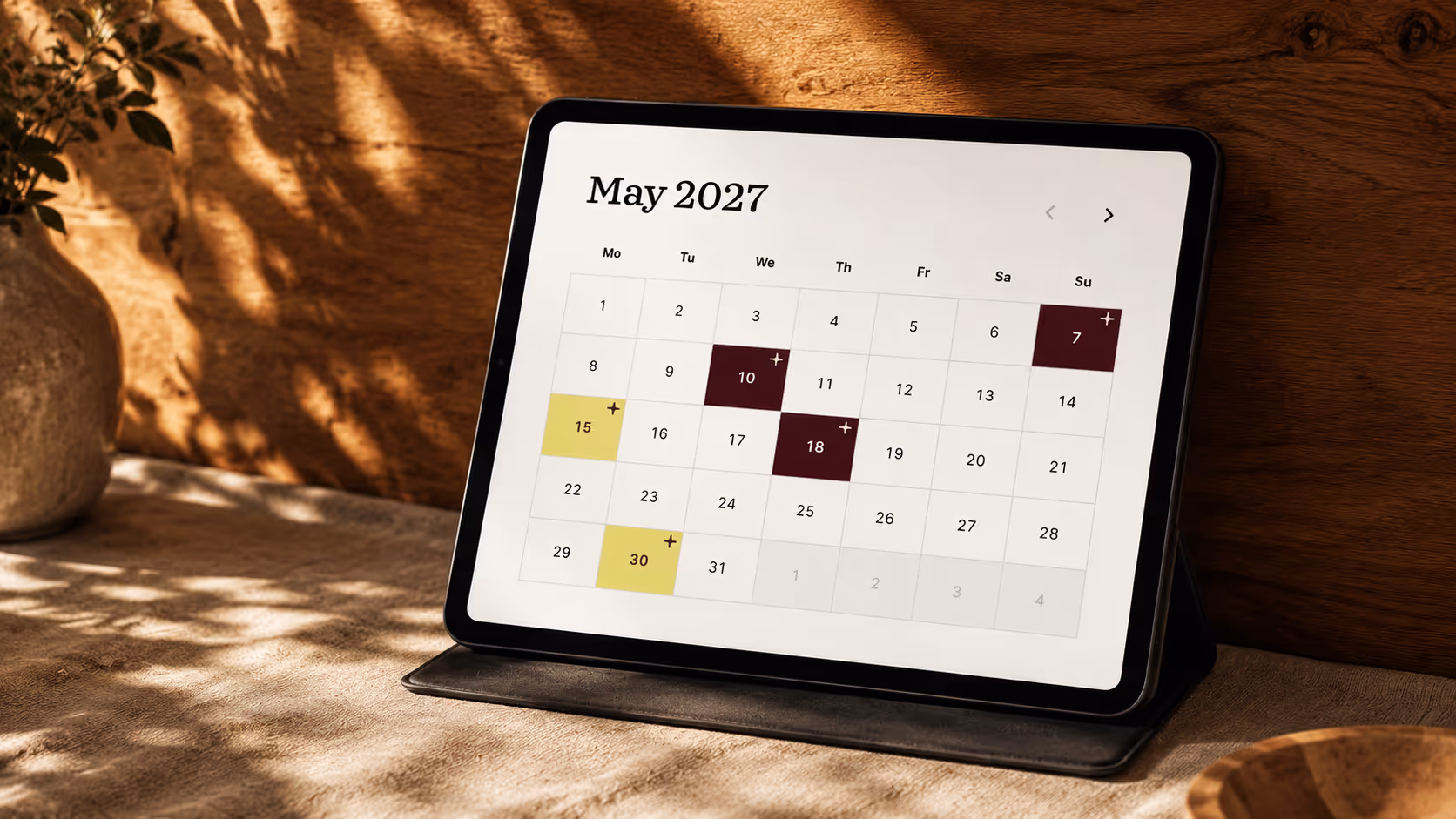 Tablet on a stand displaying a May 2027 calendar with highlighted dates 7, 10, 15, 18, and 30.