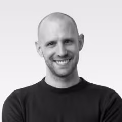 Smiling bald man with light facial hair wearing a black shirt against a plain light background.