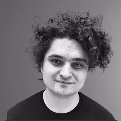 Black and white portrait of a young man with curly hair smiling slightly, wearing a dark shirt against a plain background.
