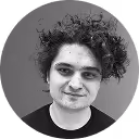 Black and white headshot of a person with curly hair smiling slightly in front of a plain background.