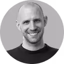 Smiling bald man with a beard wearing a black shirt against a gray background.