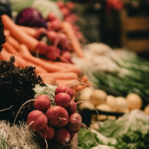 Close-up of fresh radishes, carrots, and leafy greens at a market stall.