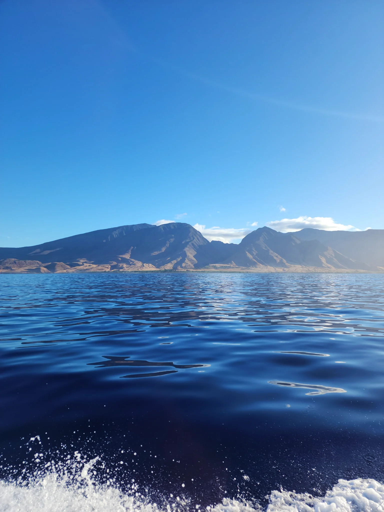Calm blue ocean with distant rugged mountains under a clear bright blue sky.