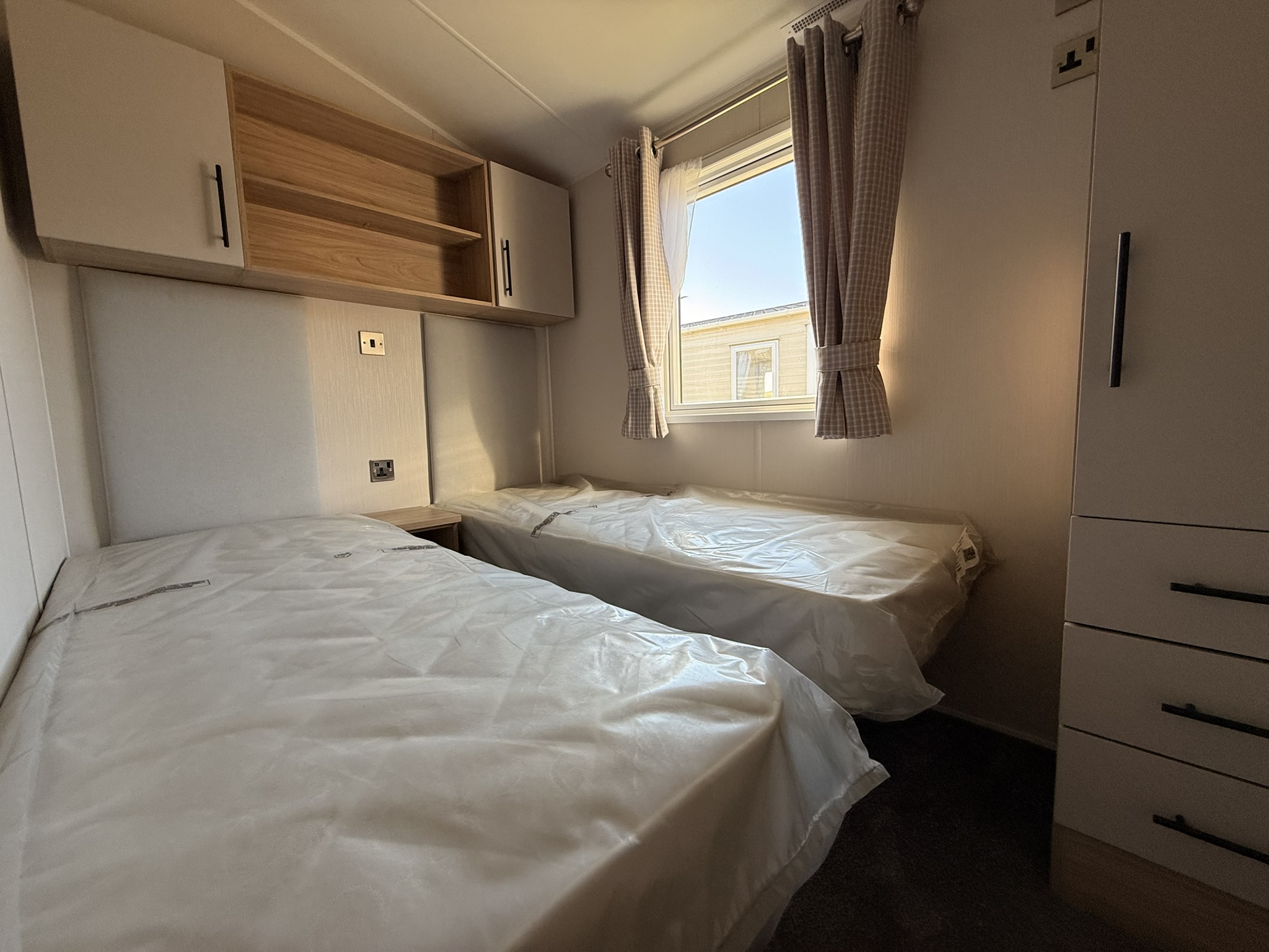 Small modern caravan bedroom with two beds, window, wooden cabinets, and storage.