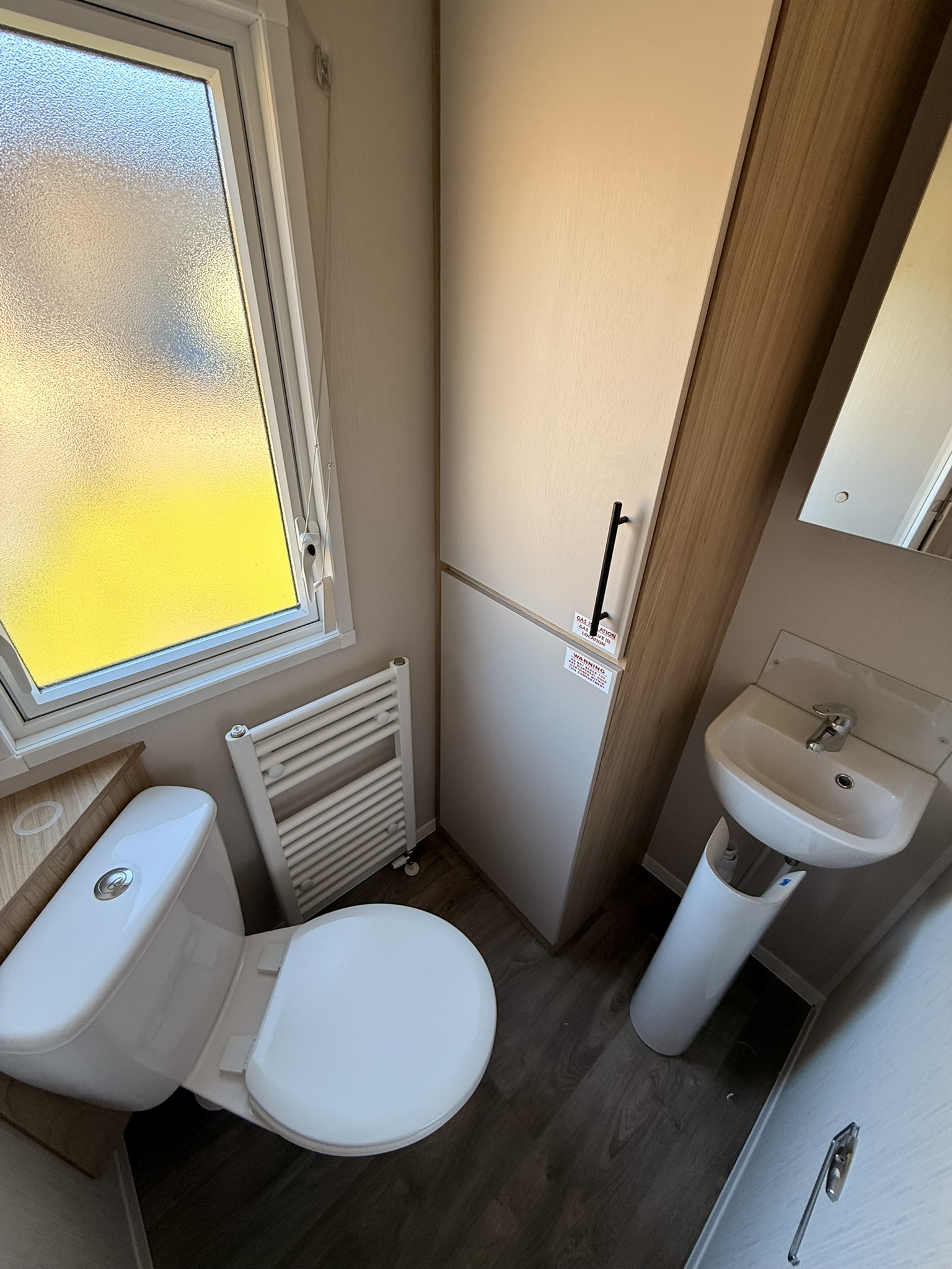 Bright modern bathroom with white toilet, pedestal sink, radiator, and frosted glass window