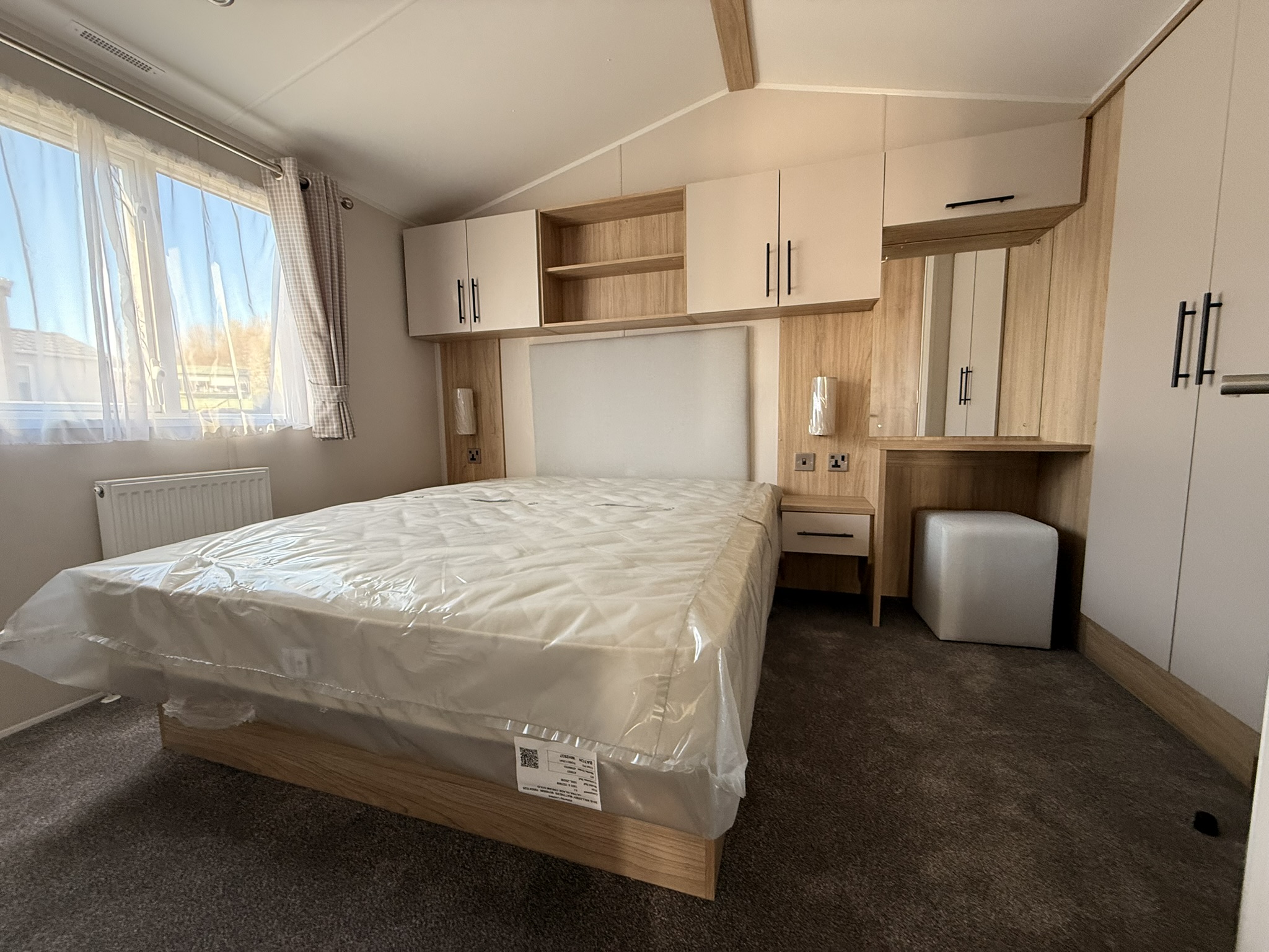 Modern bedroom with built-in wooden cabinetry, double bed, and bright window overlooking natural landscape.
