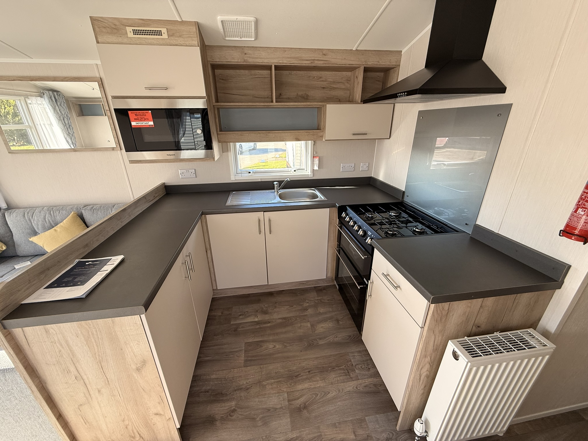 Modern caravan kitchen interior with gas cooker, sink, and wooden cabinetry.