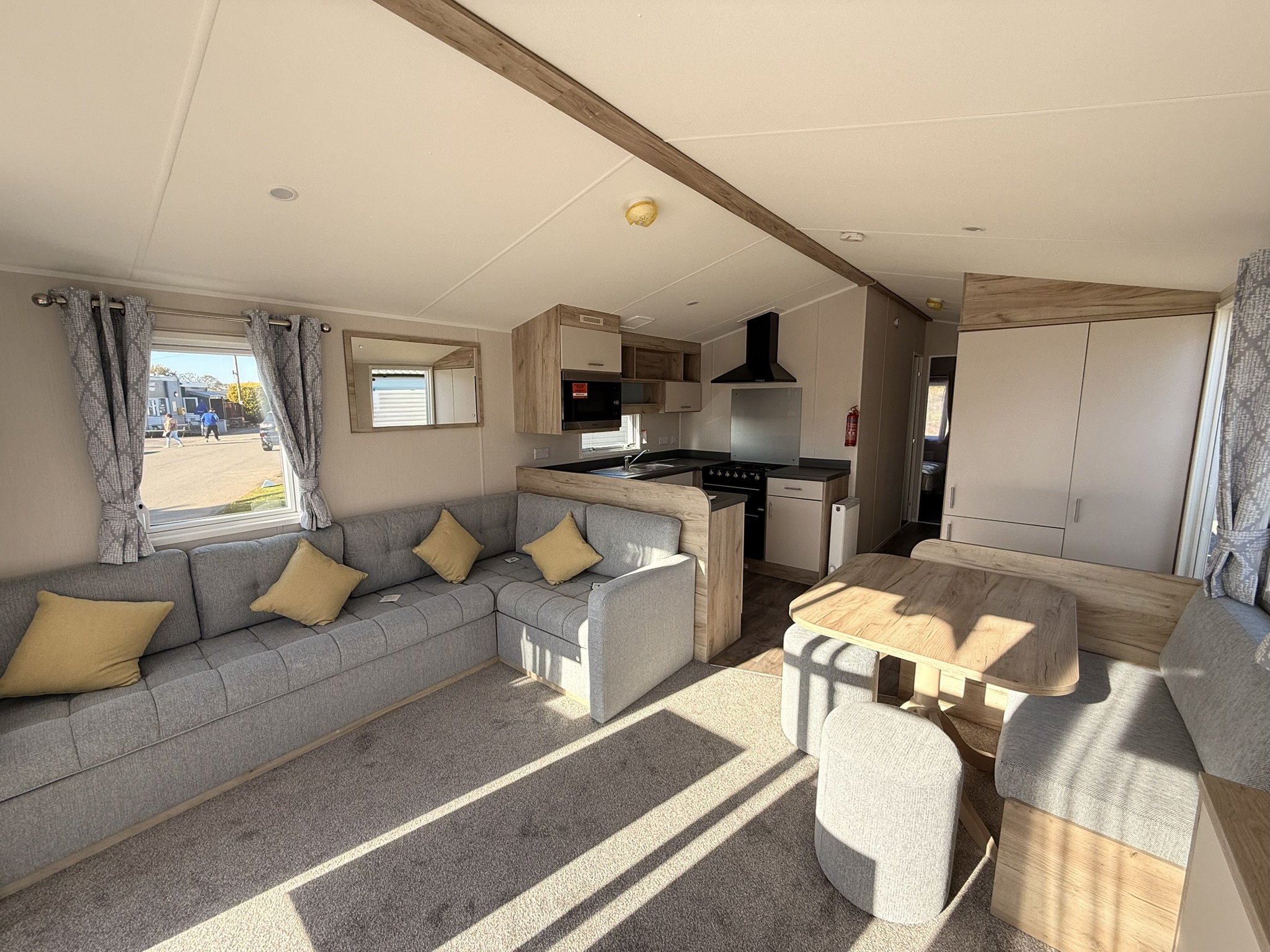 Modern mobile home interior with grey sofa, kitchen area, and wooden accents throughout